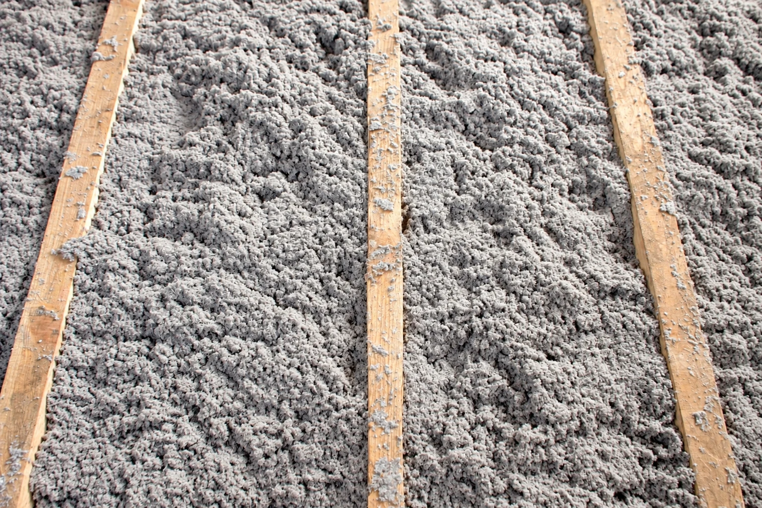Close view of loose gray blown-in insulation filling the spaces between wooden attic joists.