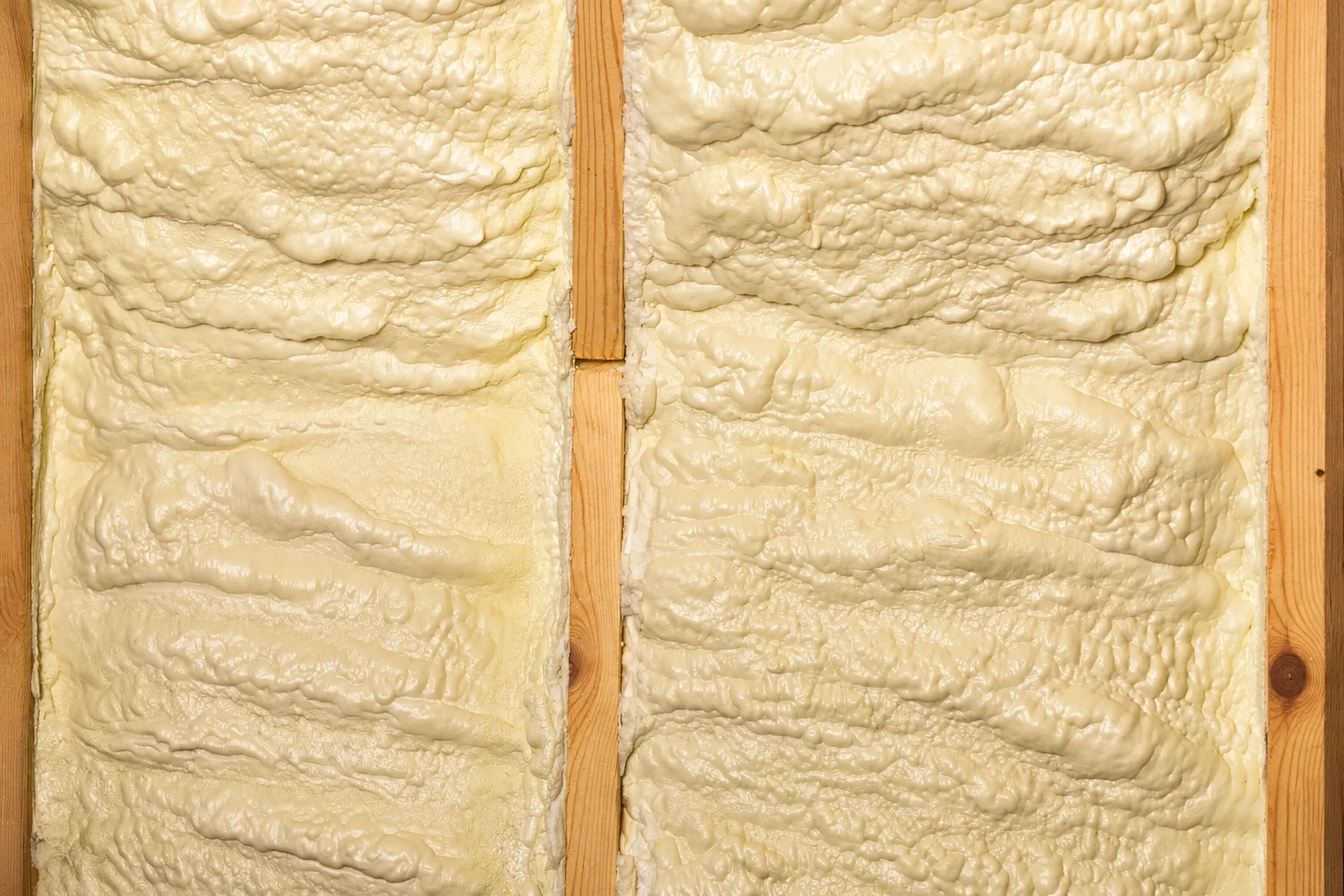 Thick cream-colored spray foam fills the spaces between exposed wooden wall studs.